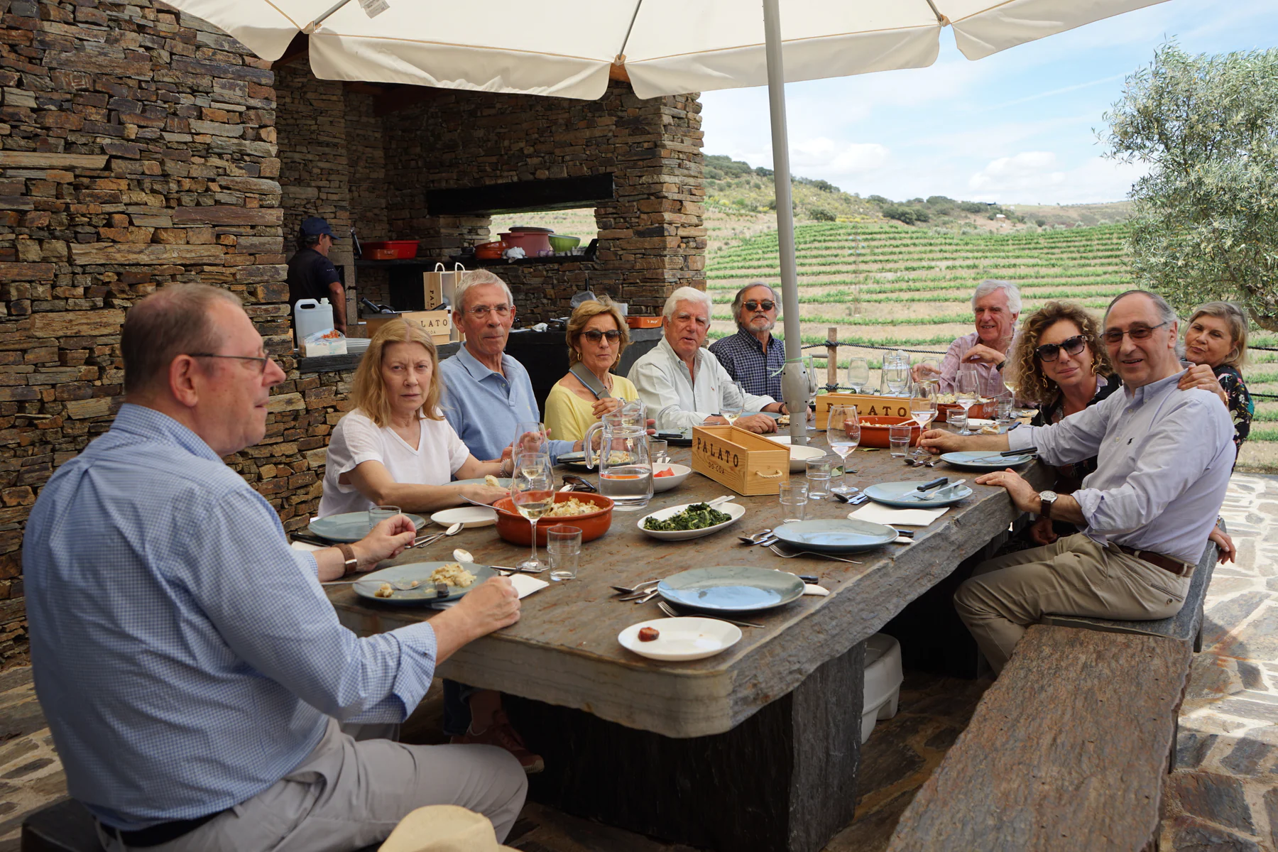 Amigos reunidos para almoçar à mesa de pedra, diante da vinha